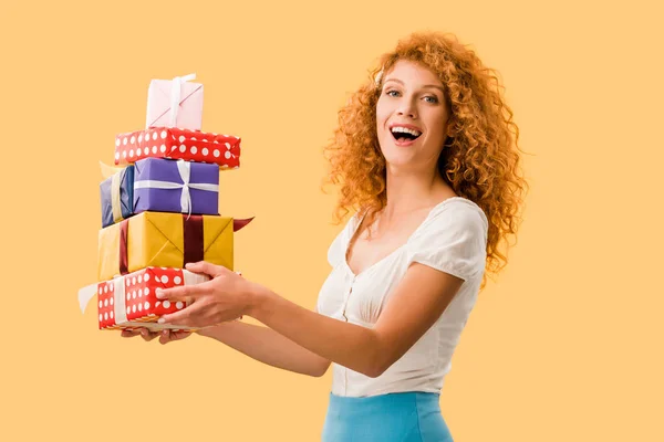 Возбужденная рыжая девушка держит подарки изолированы на желтый — стоковое фото