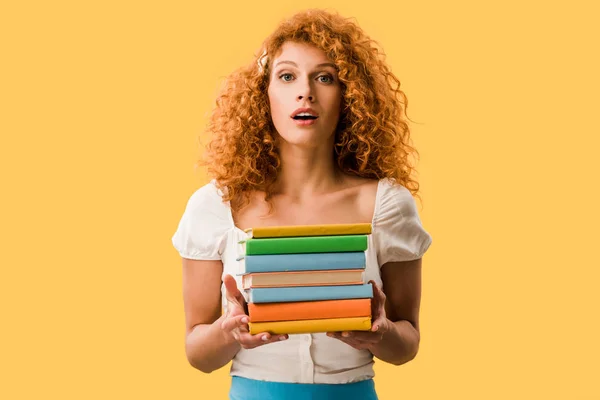 Atractivo estudiante sorprendido sosteniendo libros aislados en amarillo - foto de stock
