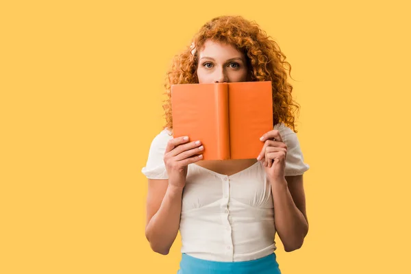 Estudante ruiva atraente com livro isolado em amarelo — Fotografia de Stock