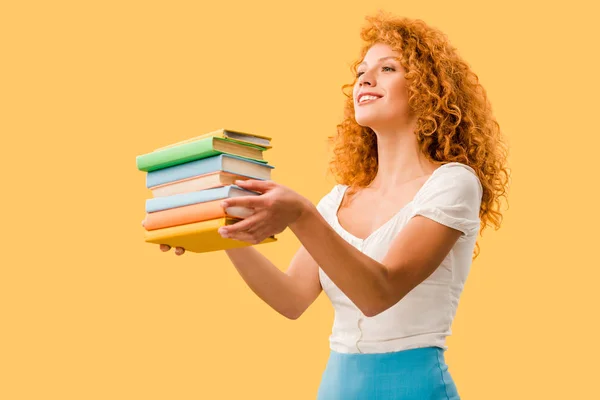 Atractivo estudiante sonriente sosteniendo libros aislados en amarillo - foto de stock