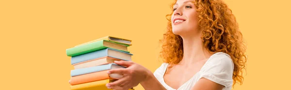 Счастливая рыжая студентка держит книги изолированы на желтый — стоковое фото
