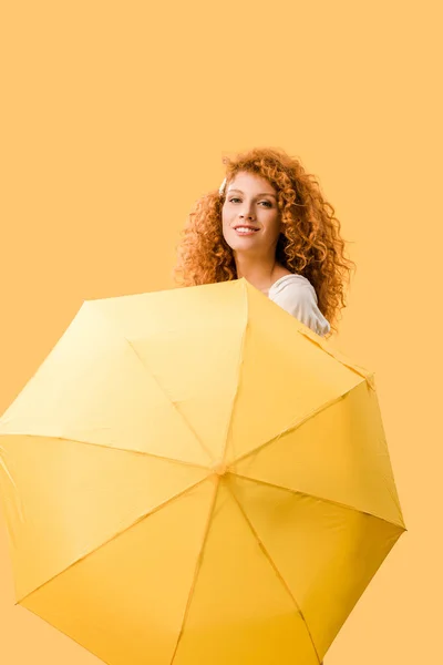 Feliz pelirroja posando con paraguas aislado en amarillo - foto de stock
