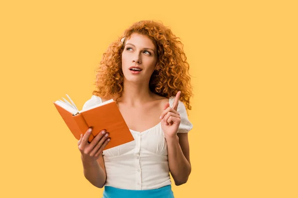 Nachdenkliche rothaarige Frau mit Buch isoliert auf gelb — Stockfoto