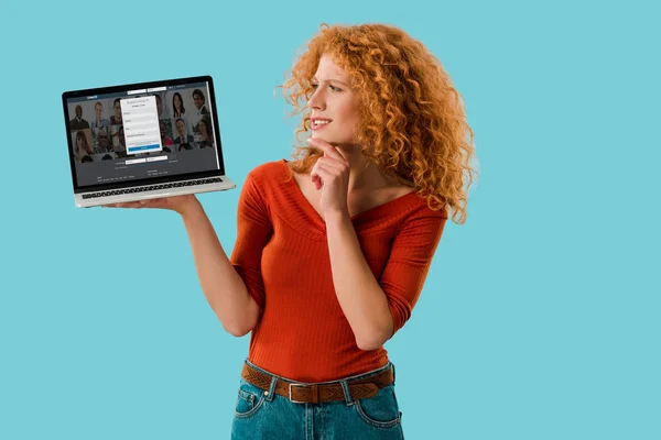 KYIV, UKRAINE - JULY 16, 2019: pensive redhead woman holding laptop with linkedin website, isolated on blue — Stock Photo