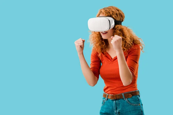 Рыжая эмоциональная женщина в гарнитуре виртуальной реальности, изолированная на голубом — стоковое фото