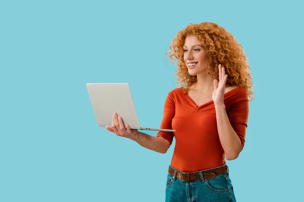 Souriant fille agitant et ayant appel vidéo sur ordinateur portable isolé sur bleu — Photo de stock