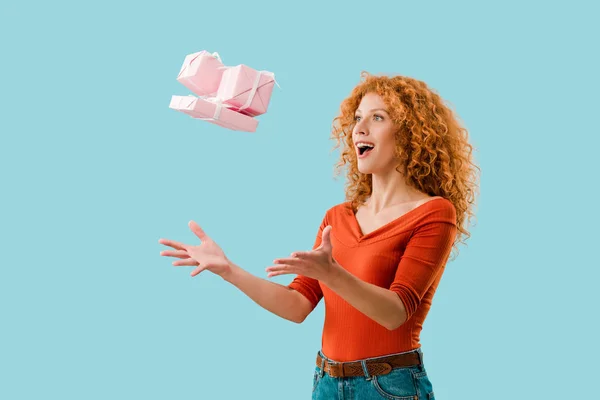 Excited redhead girl throwing up gifts isolated on blue — Stock Photo