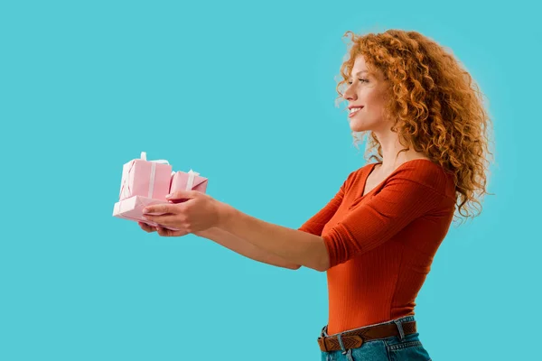 Curly redhead woman holding gifts isolated on blue — Stock Photo