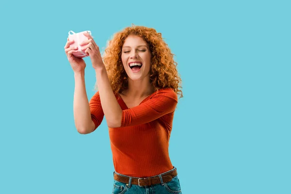 Excited redhead woman with gift box isolated on blue — Stock Photo