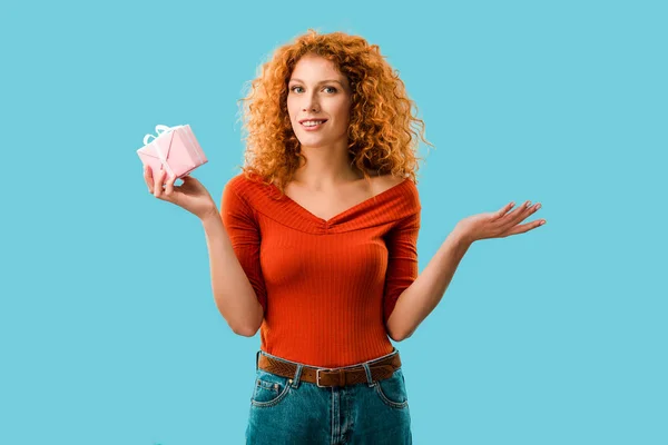 Smiling curly woman with gift box isolated on blue — Stock Photo