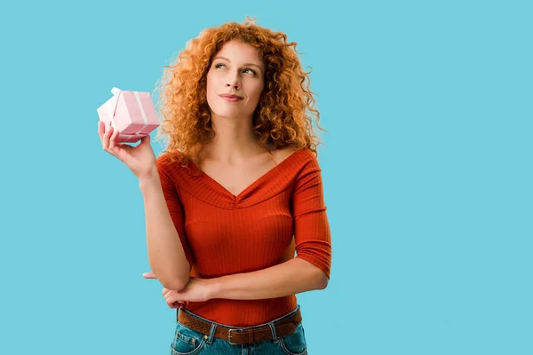 Pensive redhead woman with gift box isolated on blue — Stock Photo