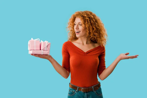 Attractive redhead woman holding pink gifts isolated on blue — Stock Photo