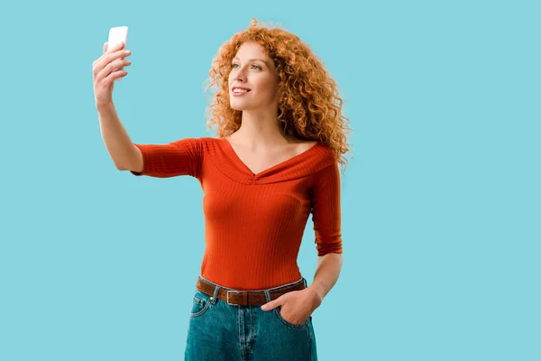 Sonriente mujer tomando selfie en teléfono inteligente aislado en azul - foto de stock
