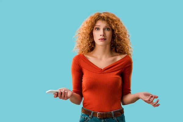 Curly confused woman holding smartphone isolated on blue — Stock Photo