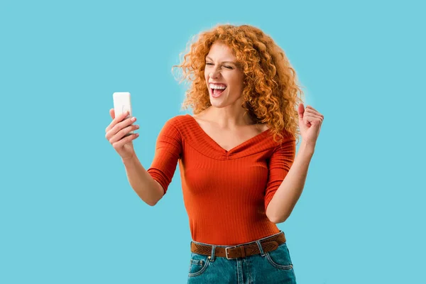 Успешная рыжая женщина с помощью смартфона изолированы на синий — стоковое фото