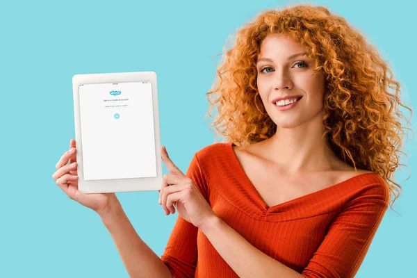 KYIV, UKRAINE - JULY 16, 2019: smiling redhead woman holding digital tablet with skype app, isolated on blue — Stock Photo