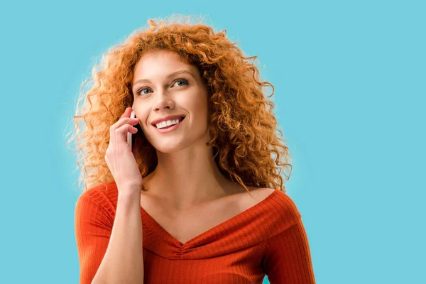 Encaracolado sorridente mulher falando no smartphone isolado no azul — Fotografia de Stock