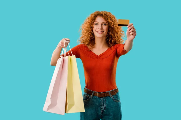 Chica feliz sosteniendo bolsas de compras y tarjeta de crédito, aislado en azul - foto de stock