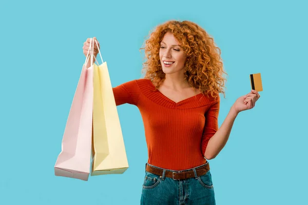 Hermosa chica sosteniendo bolsas de compras y tarjeta de crédito, aislado en azul - foto de stock