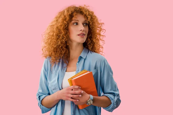 Schöne nachdenkliche Studentin hält Bücher isoliert auf rosa — Stockfoto