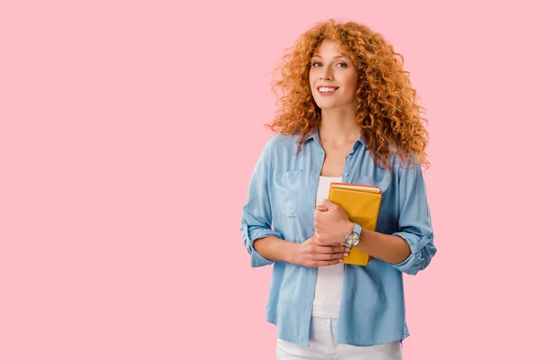 Hermoso estudiante sonriente sosteniendo libros aislados en rosa - foto de stock