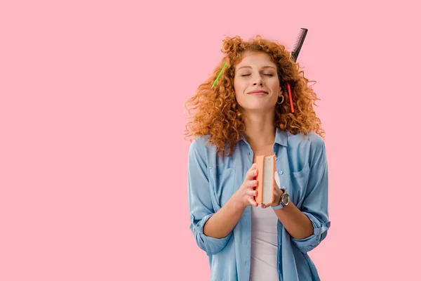 Dreamy student with pencils in hair holding book isolated on pink — Stock Photo