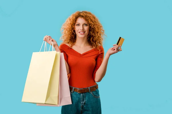 Mujer sonriente sosteniendo bolsas de compras y tarjeta de crédito, aislado en azul - foto de stock