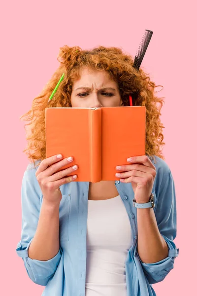 Estudiante femenina concentrada con lápices en libro de tenencia de cabello aislado en rosa - foto de stock