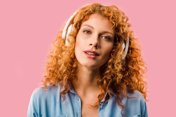 Rothaarige Frau hört Musik über Kopfhörer, isoliert auf rosa — Stockfoto