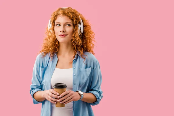 Rousse femme avec café pour aller écouter de la musique dans les écouteurs, isolé sur rose — Photo de stock