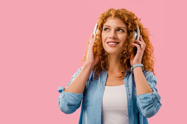 Sonriente chica rizada escuchando música en los auriculares, aislado en rosa — Stock Photo