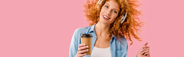 Rousse femme avec café pour aller danser et écouter de la musique dans les écouteurs, isolé sur rose — Photo de stock