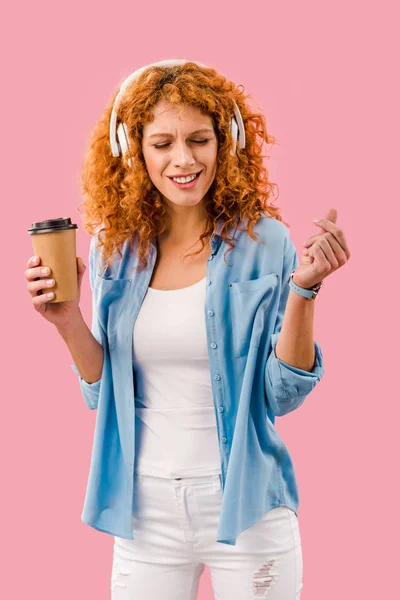 Chica atractiva con café para ir a bailar y escuchar música en auriculares, aislado en rosa - foto de stock
