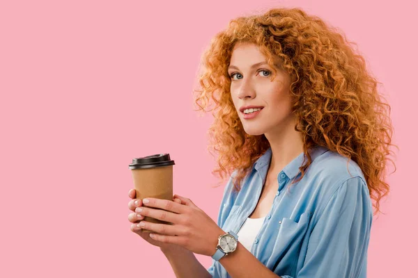 Menina encaracolado atraente com cabelo vermelho segurando café para ir, isolado em rosa — Fotografia de Stock