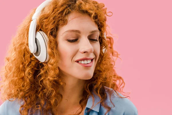Heureux rousse fille écoute de la musique dans casque, isolé sur rose — Photo de stock