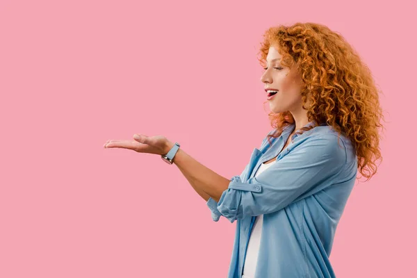 Excited redhead woman presenting something isolated on pink — Stock Photo