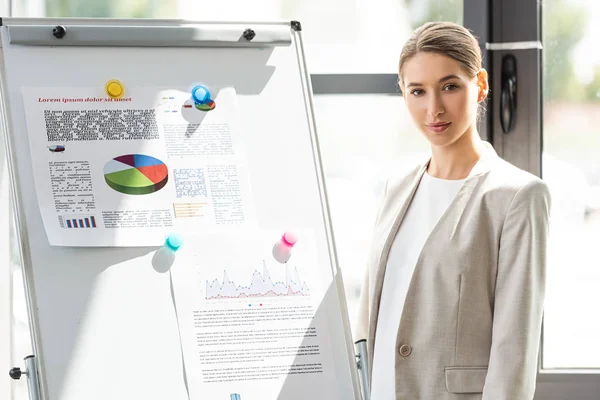 Selbstbewusste Geschäftsfrau in formaler Kleidung steht neben Flipchart mit Infografik im Büro — Stockfoto