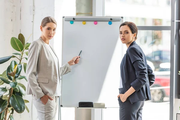 Deux femmes d'affaires en tenue de cérémonie debout près du tableau à feuilles mobiles au bureau — Photo de stock