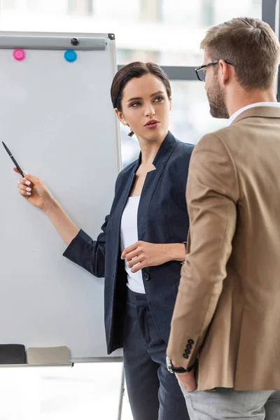 Two colleagues in formal wear standing near flipchart and looking at each other — Stock Photo