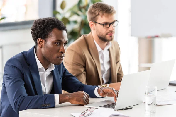 Dos hombres de negocios multiétnicos que usan computadoras portátiles en la mesa en la oficina — Stock Photo