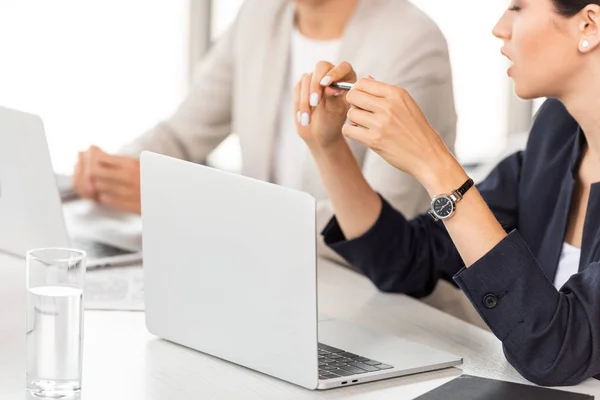 Visão parcial de duas mulheres de negócios sentadas à mesa com laptops no escritório — Fotografia de Stock