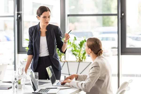 Zwei Geschäftsfrauen in formeller Kleidung, die einander anschauen und sich im Büro unterhalten — Stockfoto