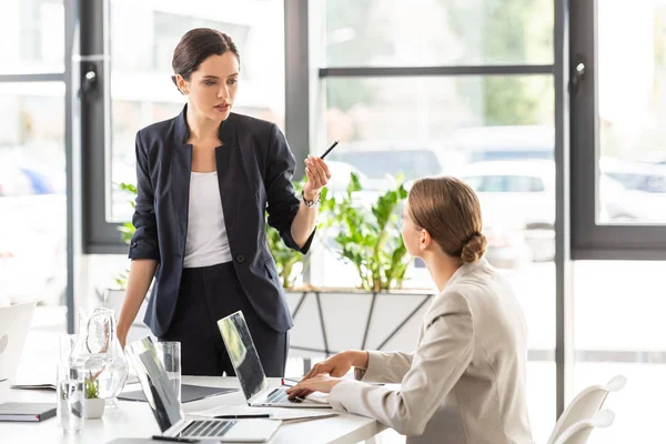 Dos mujeres de negocios en ropa formal mirándose y hablando en la oficina - foto de stock