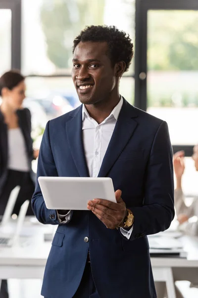 Усміхнений афроамериканський бізнесмен у формальному одязі тримає цифровий планшет в офісі — стокове фото