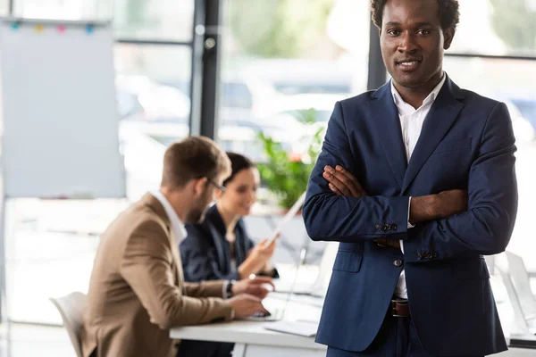 Homme d'affaires afro-américain souriant debout avec les bras croisés au bureau — Photo de stock
