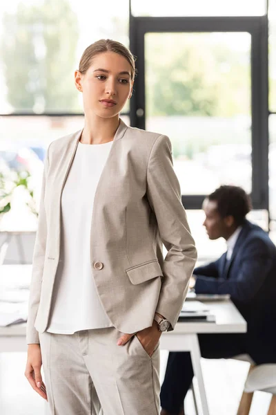 Donna d'affari pensierosa in abito formale in piedi con mano in tasca in ufficio — Foto stock