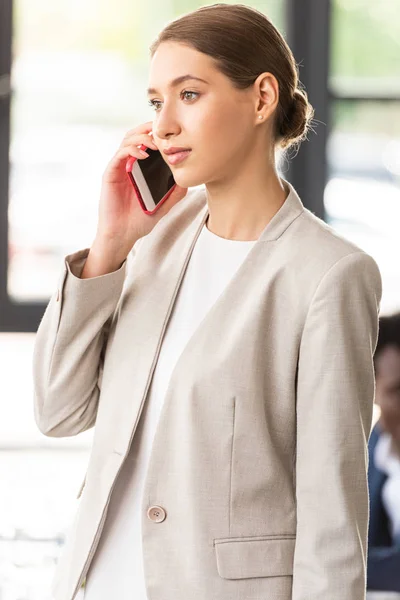 Femme d'affaires en tenue formelle parlant sur smartphone au bureau — Photo de stock