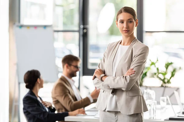 Attractive businesswoman in formal wear standing with crossed arms in office — Stock Photo