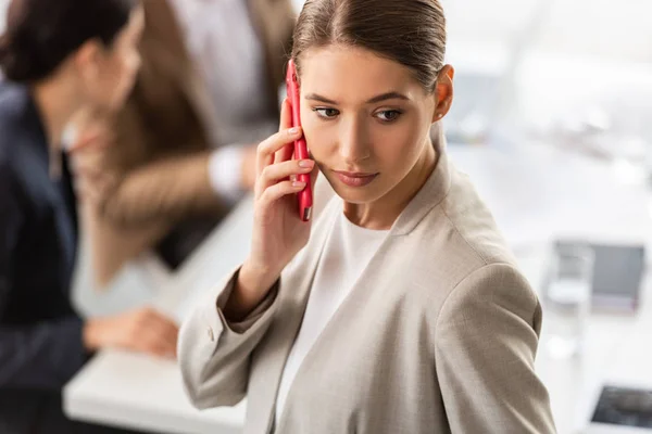 Задумчивая деловая женщина в формальной одежде разговаривает на смартфоне в офисе — стоковое фото