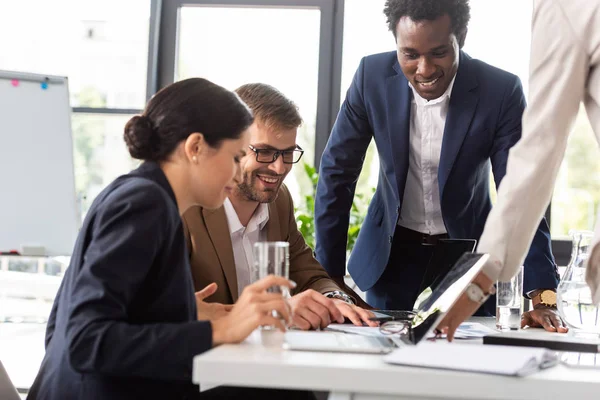 Visão parcial do sorriso de empresários multiétnicos em desgaste formal à mesa durante conferência no escritório — Fotografia de Stock